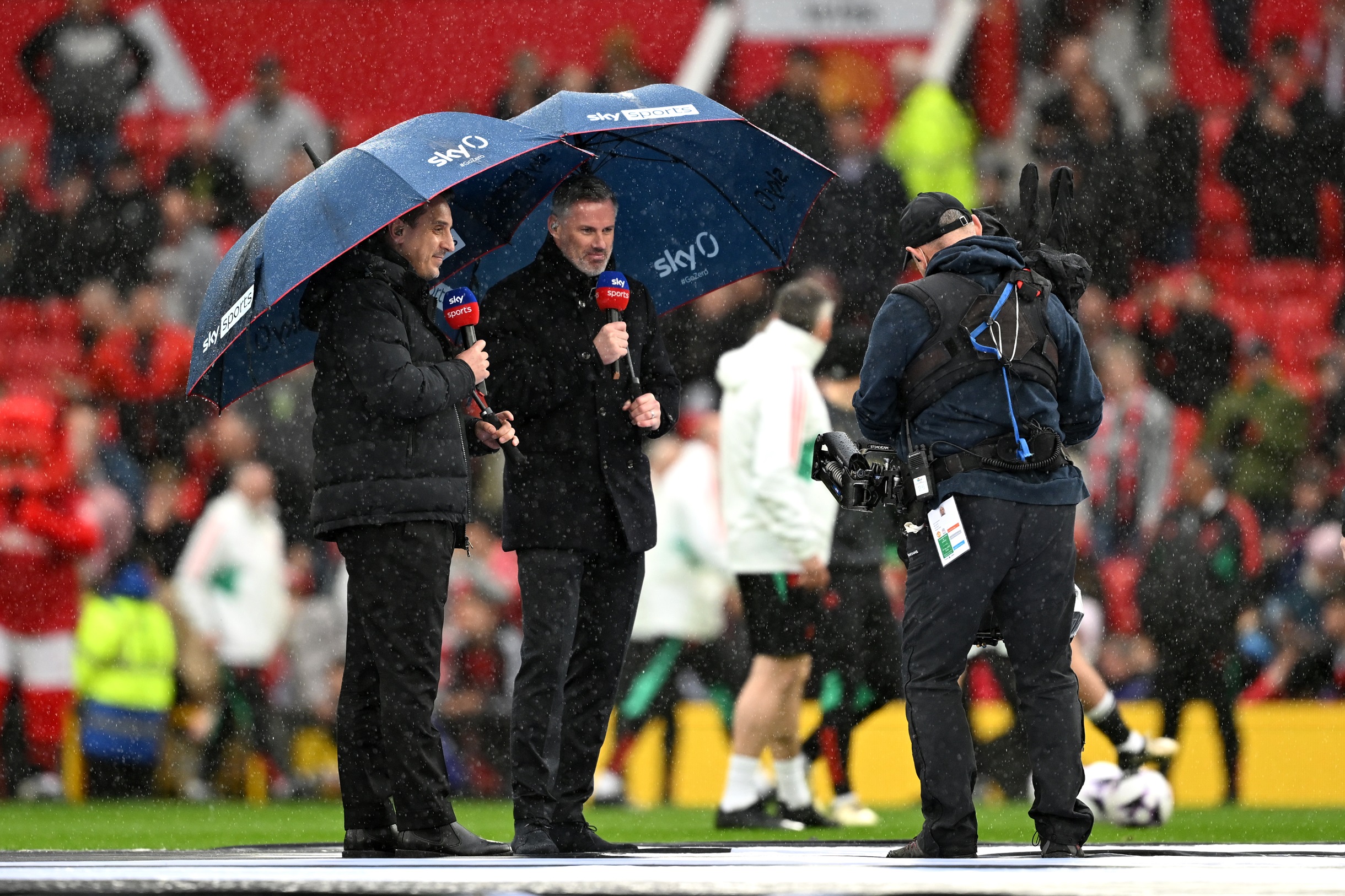 Jamie Carragher and Gary Neville stand in the pouring rain.
