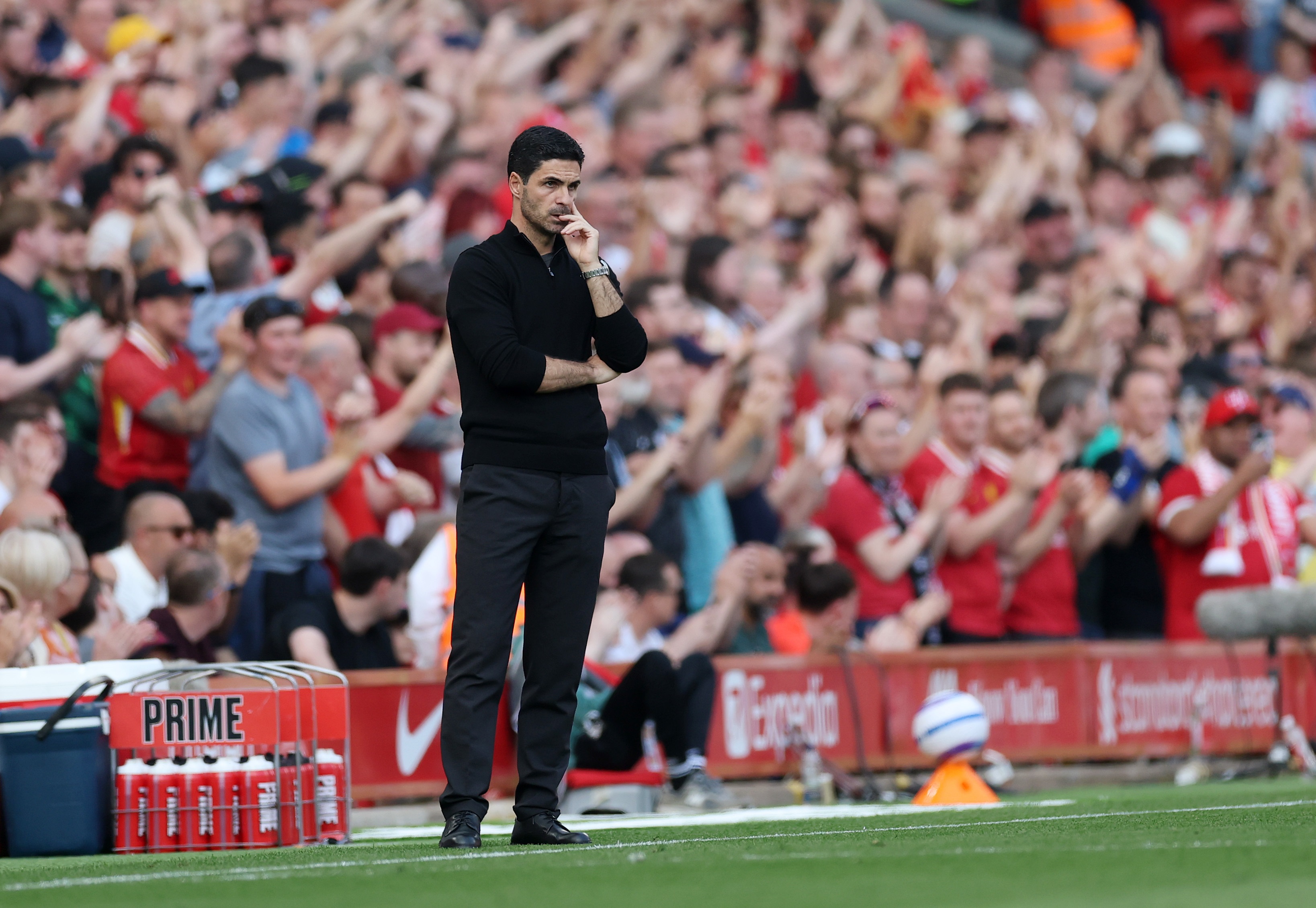 Mikel Arteta stands on the Anfield pitch with his hand covering his mouth.