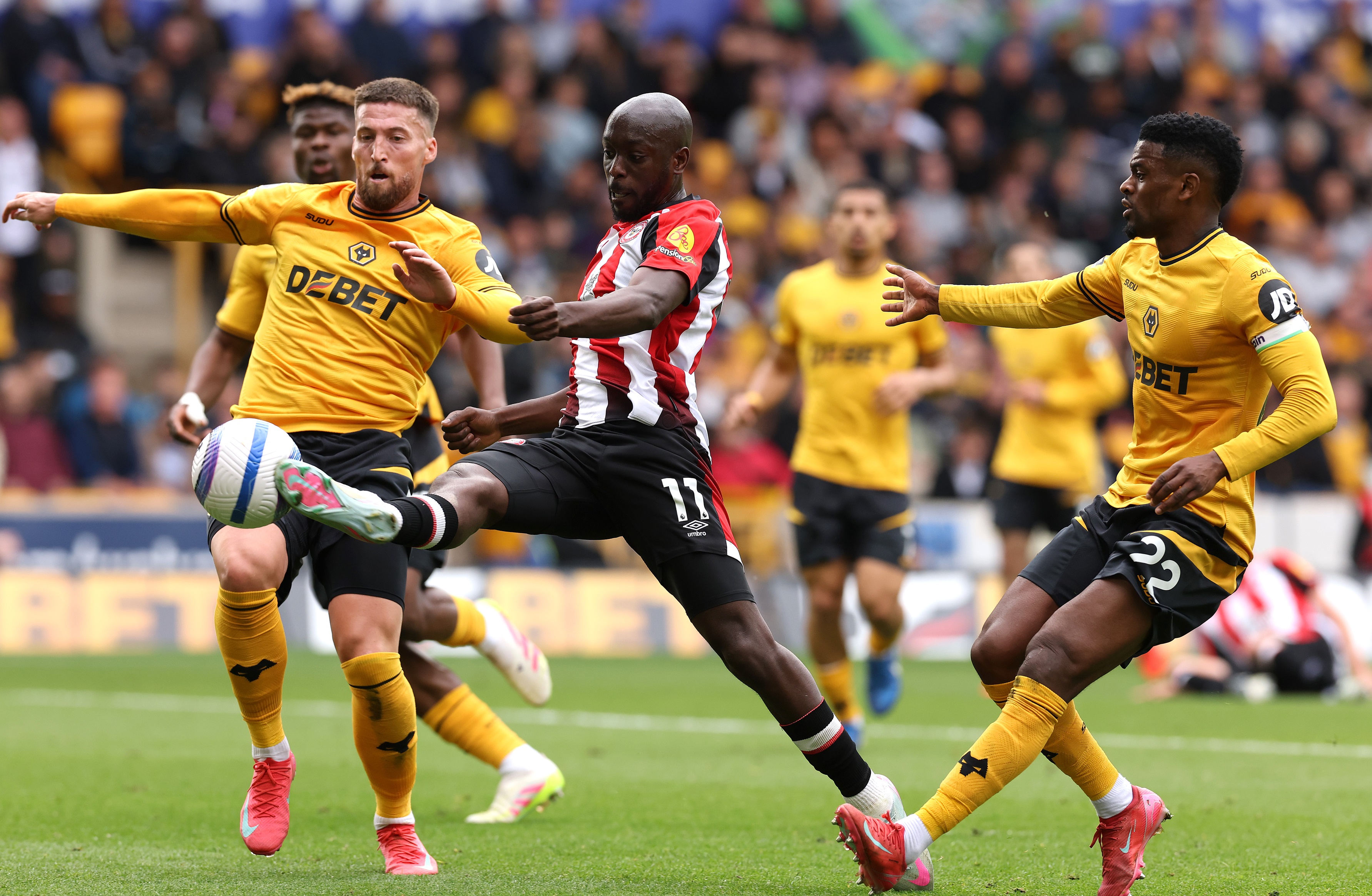 Yoane Wissa kicks the ball with an outstretched leg whilst under pressure from Wolves players.