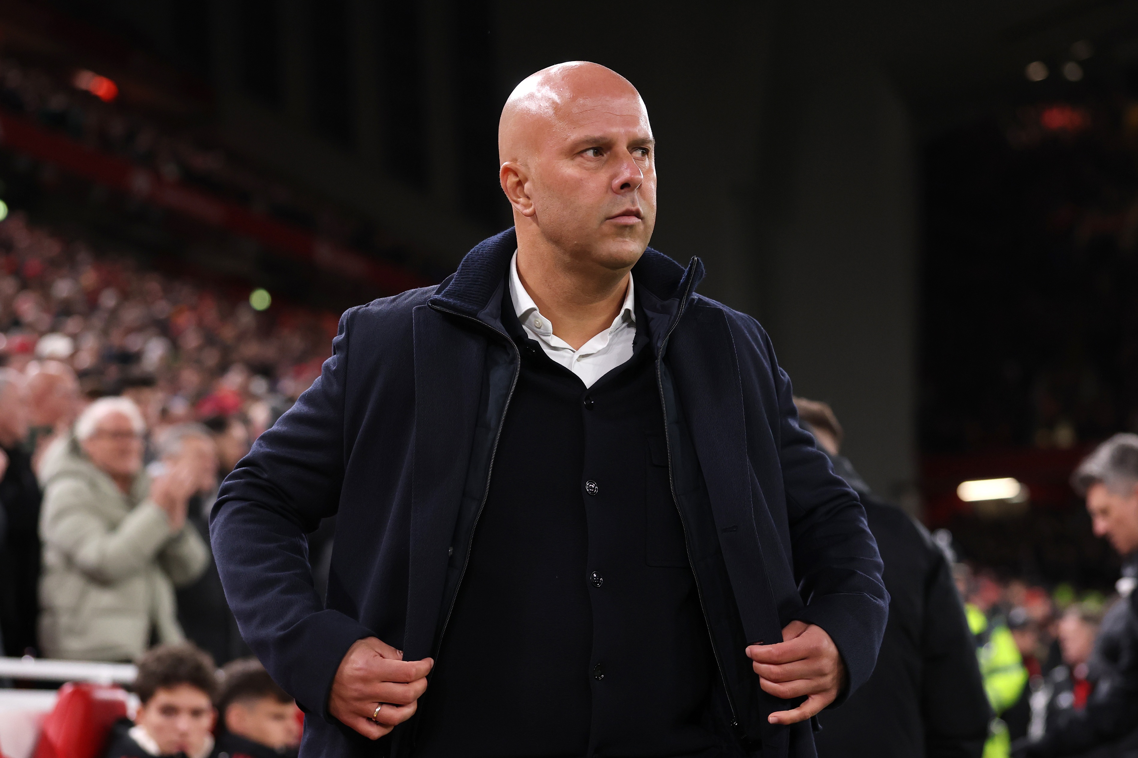 Arne Slot stands with hands on his jacket inside Anfield.