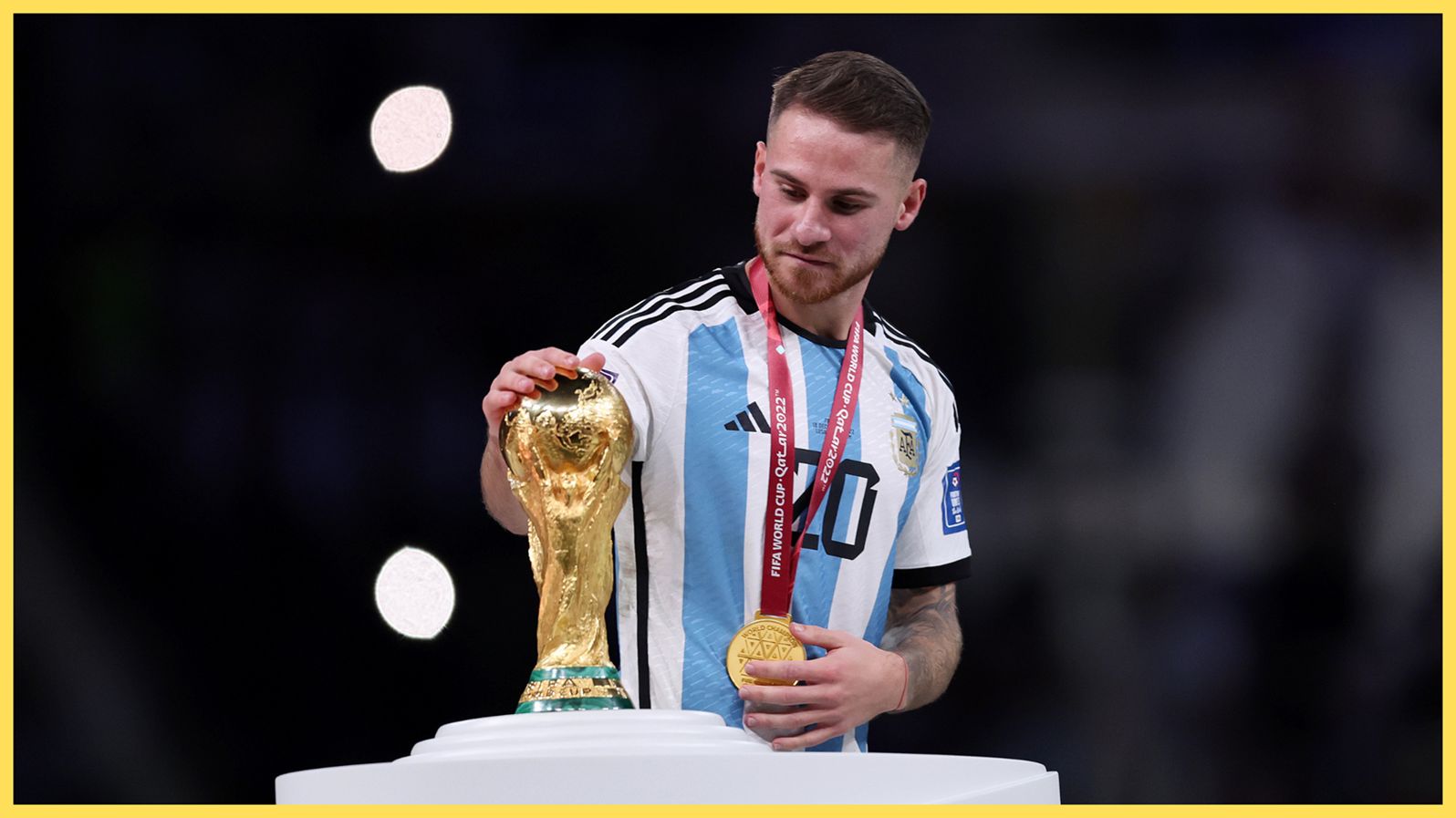 Liverpool midfielder Alexis Mac Allister places his hand on the World Cup trophy.