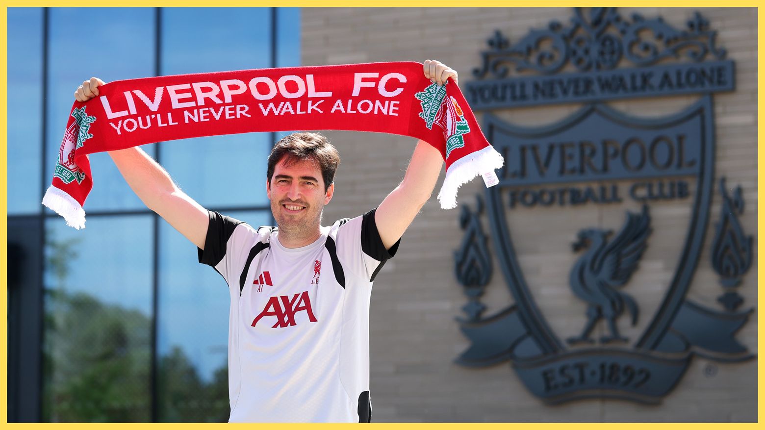 Liverpool manager Andoni Iraola smiles and holds up a LFC scarf outside the AXA training centre.