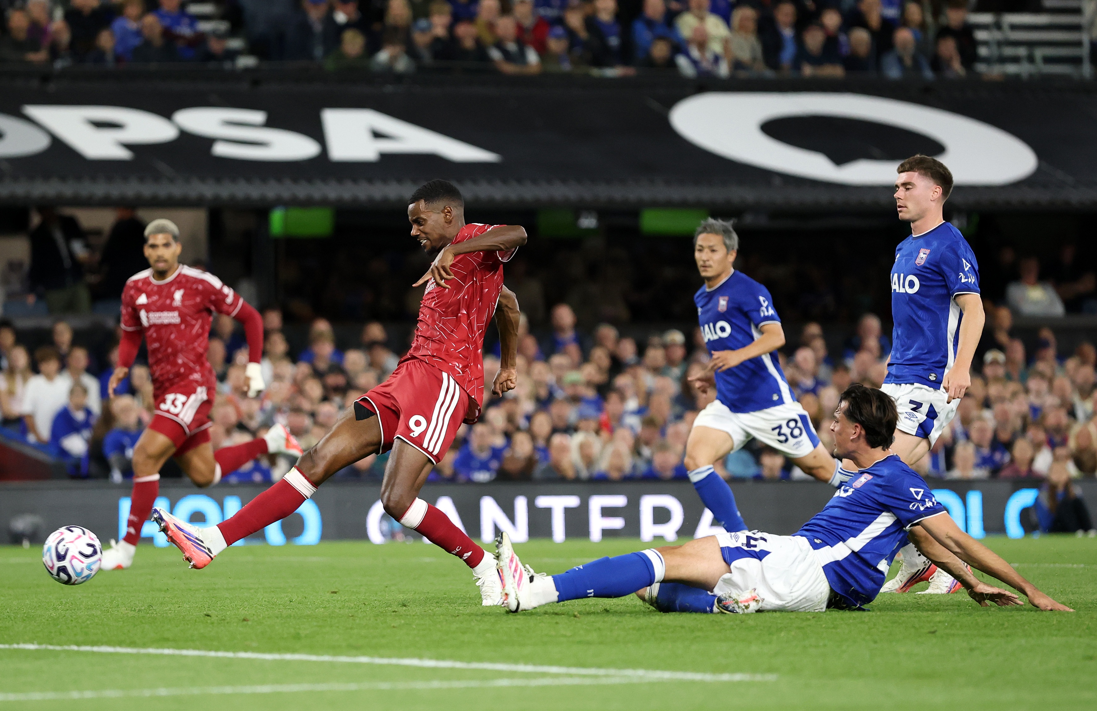 Liverpool striker Alexander Isak shoots the ball while an Ipswich players likes on the floor.