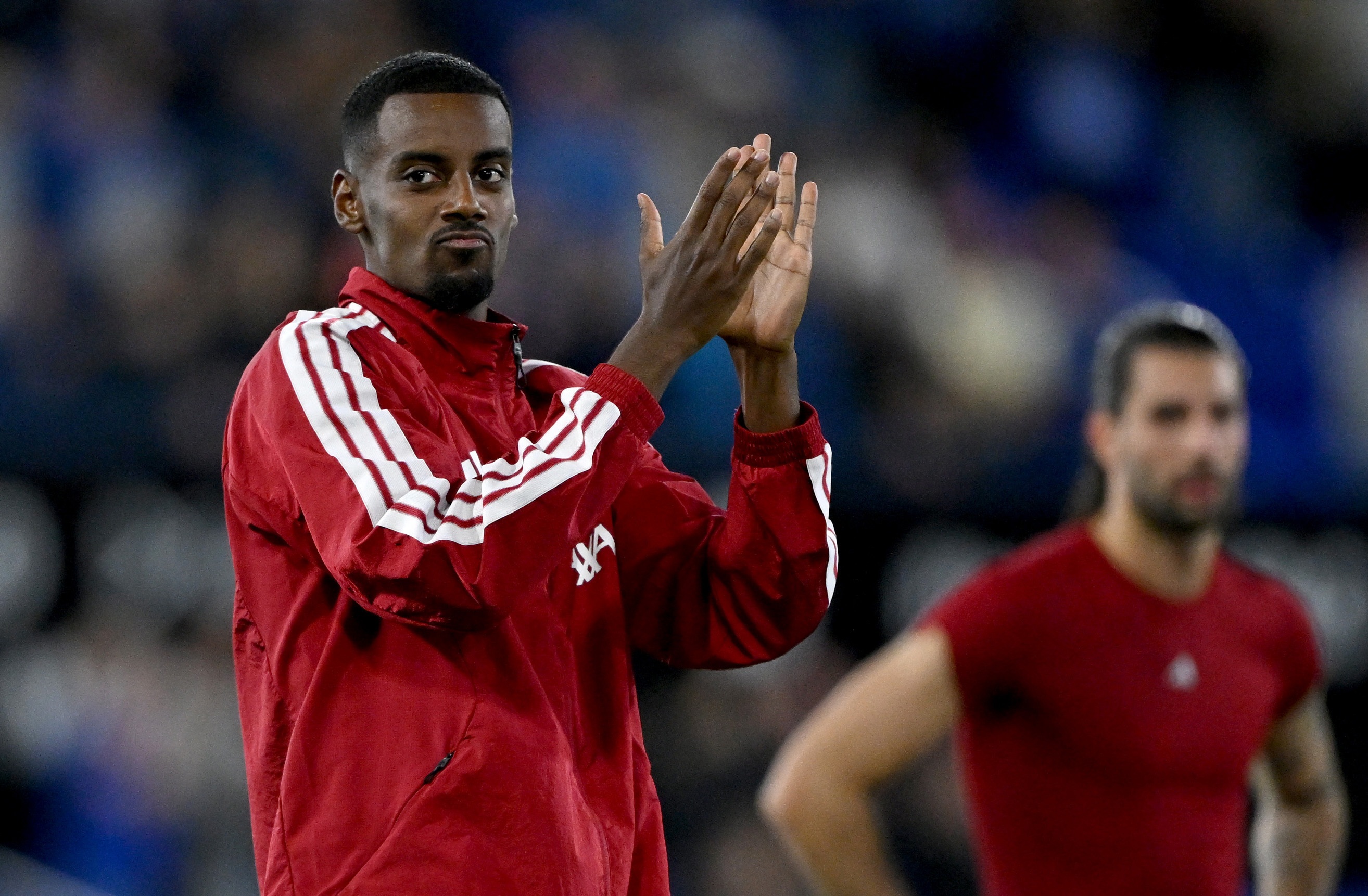 Liverpool striker Alexander Isak claps his hands while wearing red tracksuit.