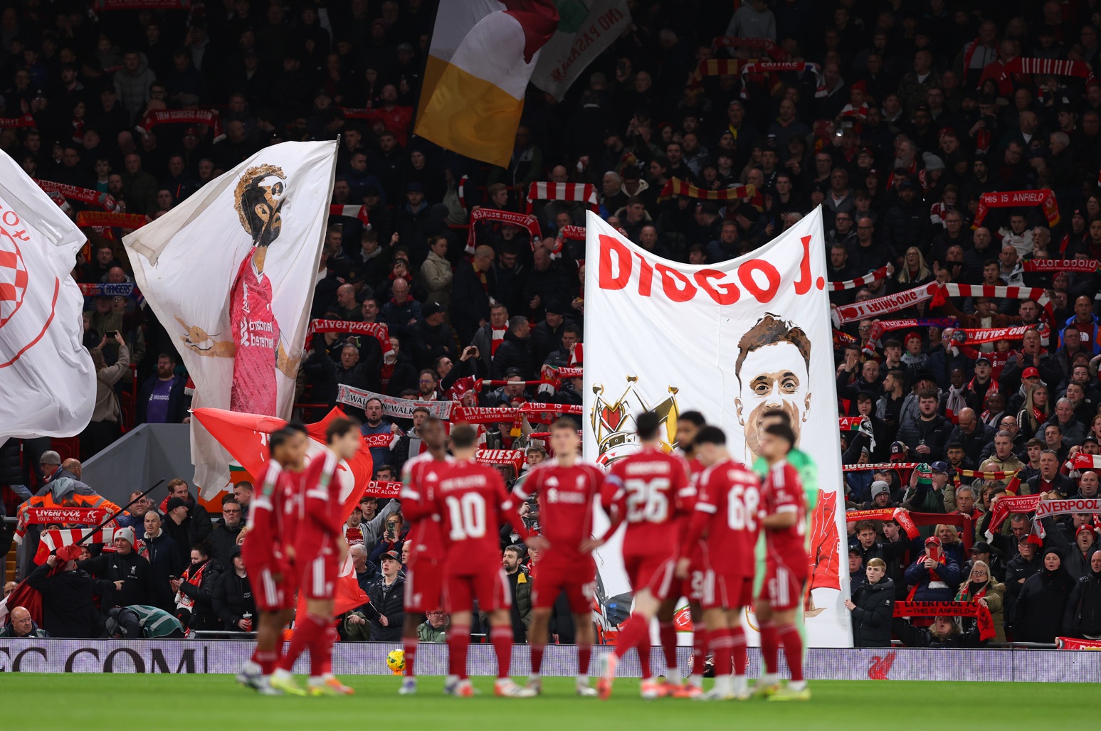 Liverpool players gather for a pre-match huddle, with a banner in tribute to Diogo Jota visible in the stands at Anfield